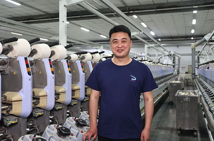 Zhang Sheng, Chief engineer at Sanyang Textile Co., Ltd., stands in front of the Autoconer 338 machine after the suction nozzle upgrade installation.