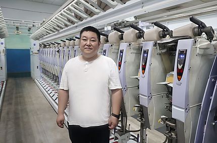 Chefingenieur Wang Ping im Werk von Wugang Longshan Textile vor Spulmaschinen Autoconer X5, die mit der Smartjet-Power-Düsentechnologie ausgerüstet wurden.